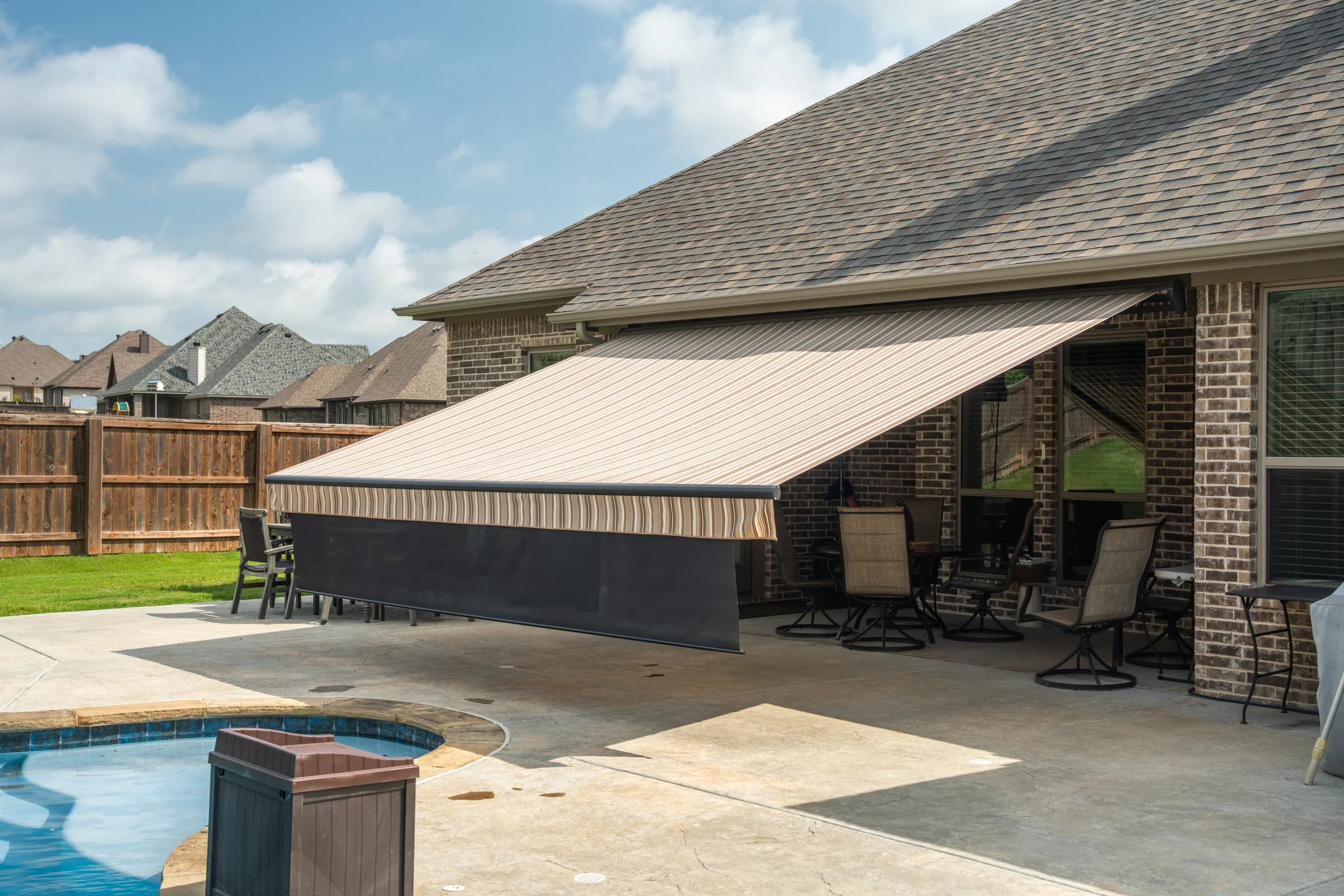 Retractable patio awning with an integrated front drop screen beside a residential pool